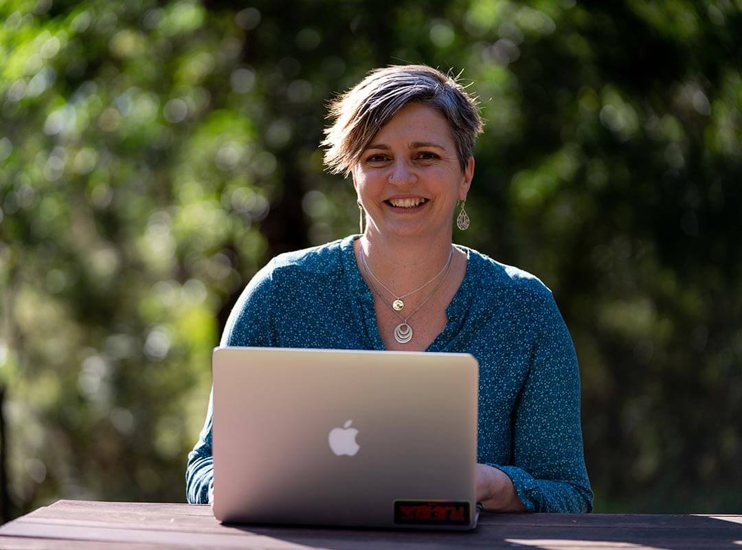 Mandy Mercuri, professional writer and novelist, sitting outside on a bench working on her laptop.